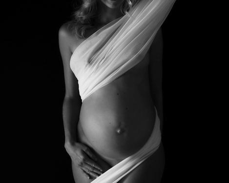 Schwangere Frau in weißes Tuch gehüllt vor schwarzem Hintergrund