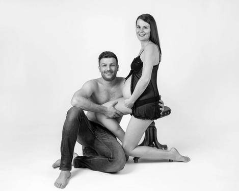Pregnant woman sitting on a stool, her partner on the floor, both looking at the camera, b&w shot