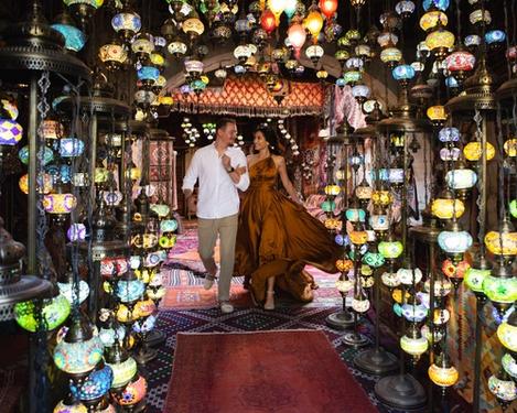A couple in love run out of a carpet shop, surrounded by many coloured lights.