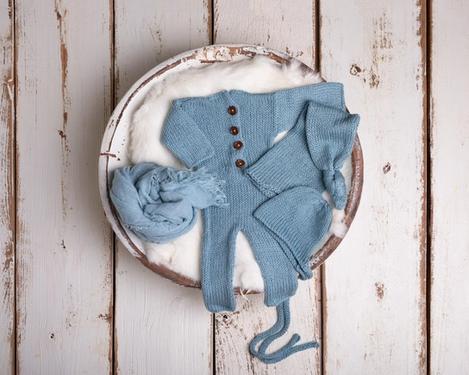 Light blue knitted romper suit with caps and shawl in a white wooden bowl for newborn photography