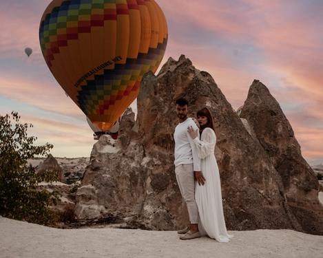 Verliebtes Paar in den Bergen bei Sonnenaufgang mit vielen Heißluftballons im Hintergrund