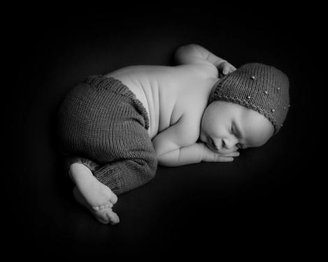 Schlafendes Baby mit Mütze und Hose auf schwarzem Hingtergrund.