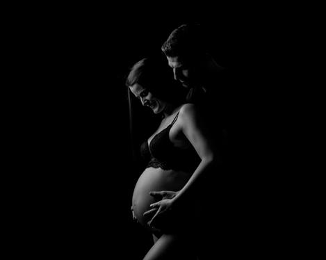 Pregnant woman with partner in side view against black backgroundet
