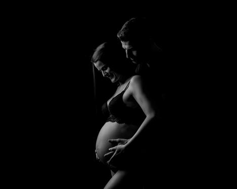 Schwangere Frau mit Partner in Seitenansicht vor schwarzem Hintergrund