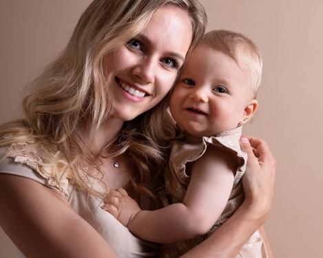 Portrait of a mother with her one-year-old baby smiling at the camera. Both are dressed in beige in a studio set of the same colour.