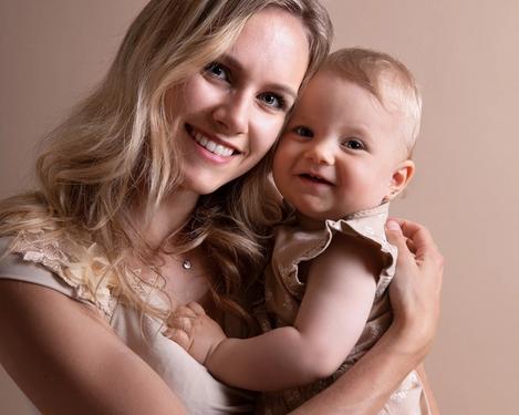 Portrait einer Mutter mit ihrem einjährigem Baby lächeln in die Kamera. Beide sind beige gekleidet in gleichfarbigem Studioset.