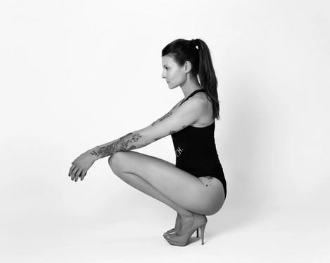 Woman squats on floor in black bikini and high heels, studio shot 