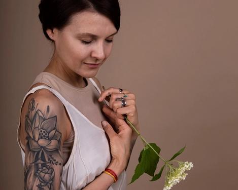 Dunkelhaarige Frau sitzt in hellem Kleid auf einem Sessel. Sie hat eine weiße Blume in der Hand ihr Blick ist nach unten gerichtet.