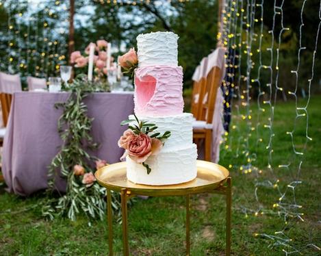 White and pink wedding cake in the foreground, the pink laid table in the background, framed by fairy lights