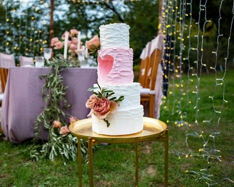 Weiß-rosa Hochzeitstorte im Vordergrund, im Hintergrund der rosa gedeckte Tisch, umrahmt von Lichterketten