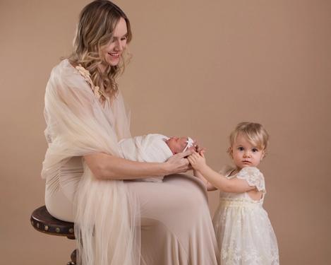 Mutter mit Kleinkind und Baby in creme farbigen Kleidern vor beigem Hintergrund