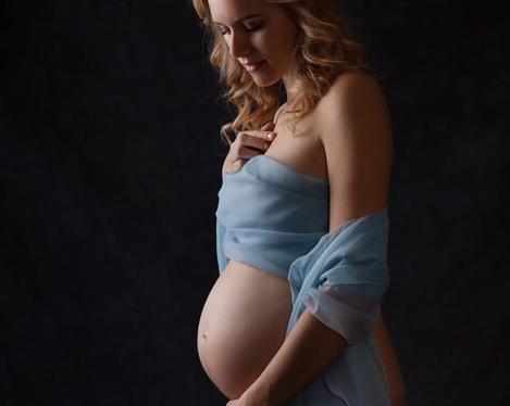 Pregnant woman in side view with light blue silk scarf in front of body