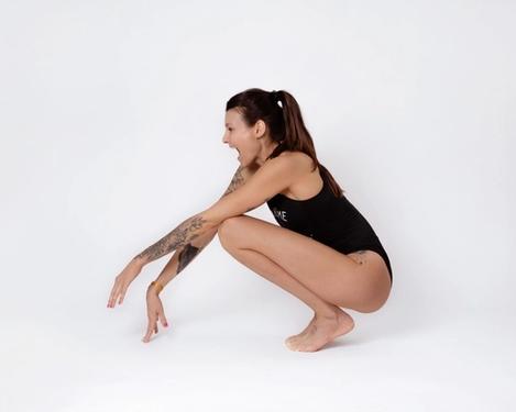Woman in black swimsuit squats on floor and laughs, studio shot