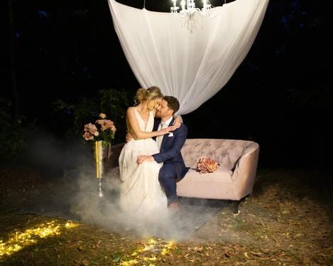 Bride and groom sitting on an antique pink armchair in the dark with fog in the foreground 