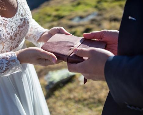 Hands of a bride and groom on a small leather booklet, in which their wedding vows are immortalized