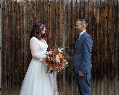 Brautpaar steht in Abstand zueinander, vor einem brauen Holztor