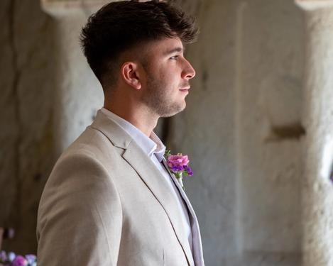 Bräutigam in hellem Anzug steht in einem sandsteinfarbenen Raum und blickt in die Ferne