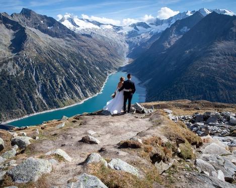 Back view of bride and groom in mountains looks down on reservoir lake