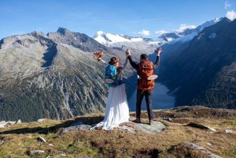 Back view of bride and groom with backpack in mountains with view of reservoir lake