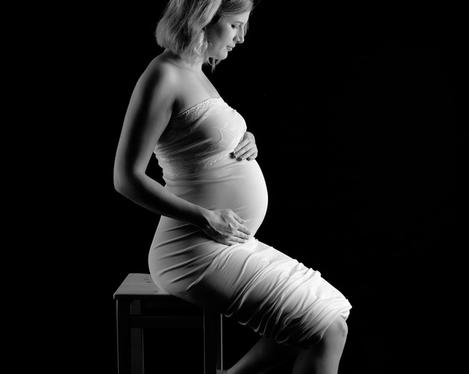 Pregnant woman in side light and tight white dress against black background