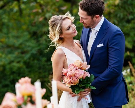 Brautpaar mit rosa Blumenstrauß in ihren Händen, im Vordergrund der gedeckte Hochzeitstisch