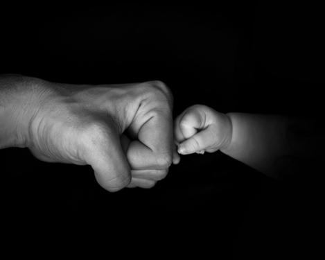 Babyfaust drückt gegen Vaters Faust auf schwarzem Hintergrund 