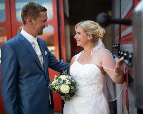 Bride smiles at groom, they stand in front of a red fire engine
