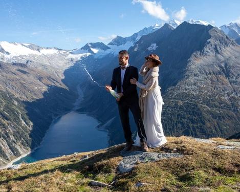 Bride and groom open a bottle of champagne in the mountains in the background you can see a reservoir