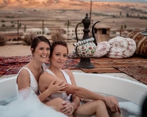 A same-sex female couple sits in an outdoor bathtub and has fun.