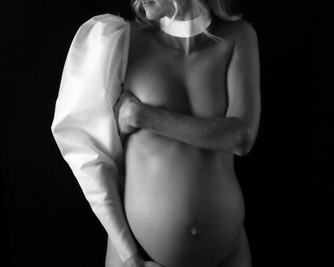 Schwangere Frau mit nur einem weißen Ärmel und Halsband bekleidet vor schwarzem Hintergrund