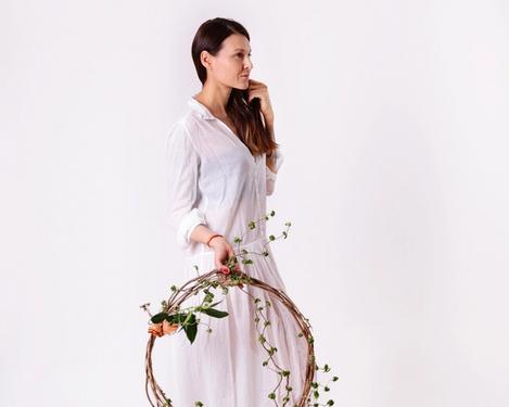 Woman in white dress holds a wreath of flowers in her hand, she looks straight ahead
