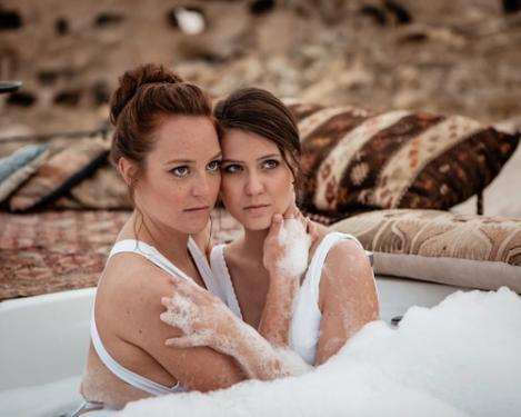 Ein gleichgeschlechtliches weibliches Paar sitzt in einer Outdoor-Badewanne und hat die Köpfe aneinander.