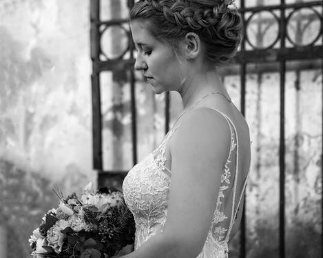 Side view of the bride looking down to the bouquet, in front of an iron gate