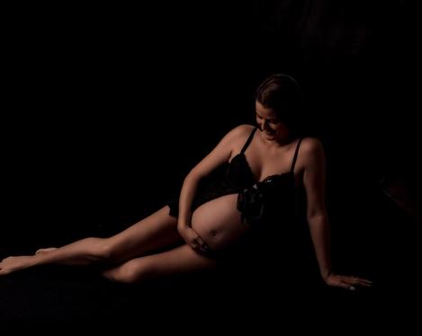 Pregnant woman sitting on the floor with legs stretched out against black background