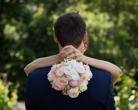 Bride holding pink bouquet over groom's back view