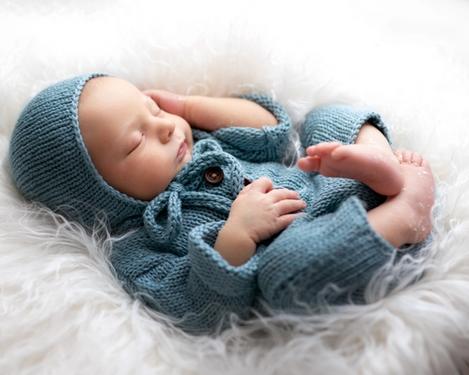 Neugeborenes in blauem Overall und Mütze schläft auf einem weißen Fell