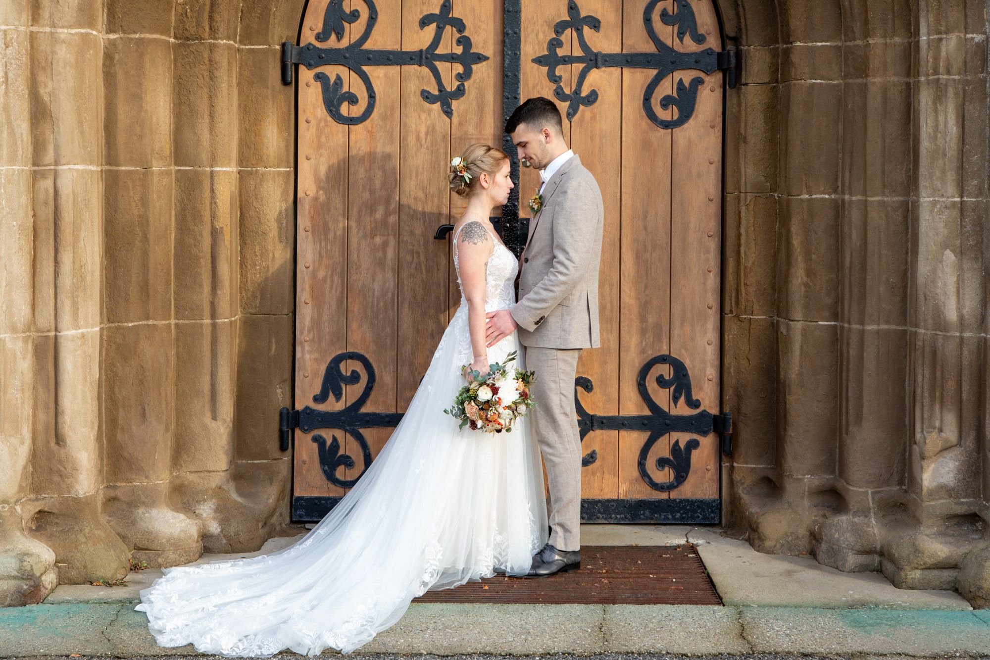 Brautpaar zueinander stehend vor einem großen braunem Holzportal