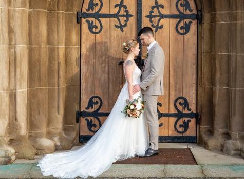 Bride and groom standing together in front of a large brown wooden portal