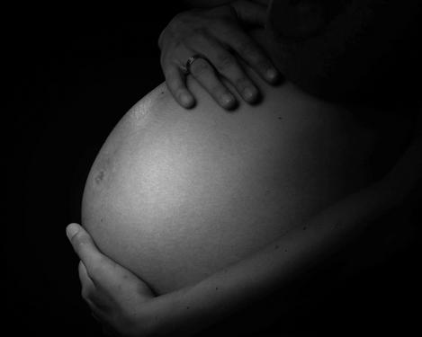 Babybauch umrahmt von beiden Händen der werdenden Mutter vor schwarzem Hintergrund