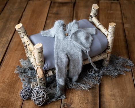 Birkenholzbettchen mit grau gestricktem Strampler mit Mütze drauf, für die Neugeborenen-Fotografie