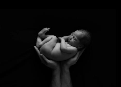 Neugeborenes, schlafendes Baby in den Händen seines Vater auf schwarzem Hintergrund
