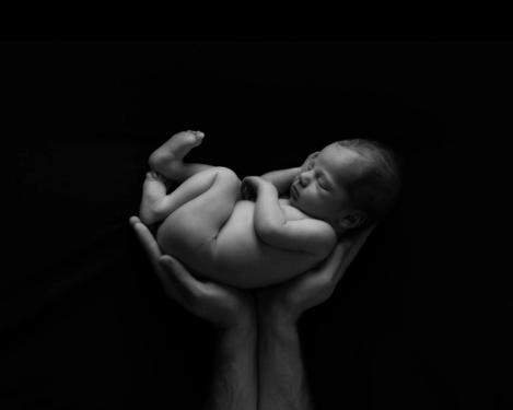 Neugeborenes, schlafendes Baby in den Händen seines Vater auf schwarzem Hintergrund
