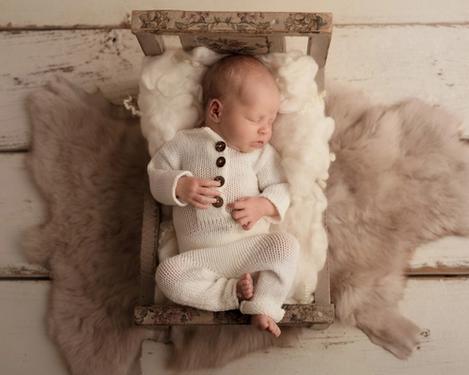 Newborn baby in white romper suit in a crib on light wooden floor