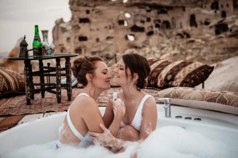 A same-sex female couple sits in an outdoor bathtub and has fun.