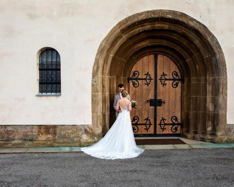 Wedding couple standing at a huge old round entrance portal, back view of the bride