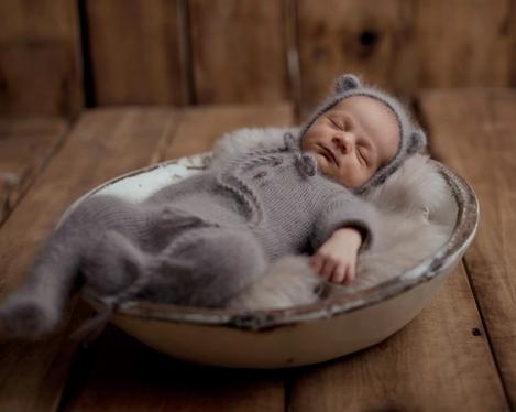 Neugeborenes in braunem Overall schläft in einer mit Fell gepolsterten weißen Schale.