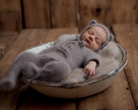 Neugeborenes in braunem Overall schläft in einer mit Fell gepolsterten weißen Schale.