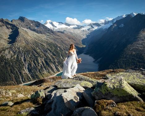 Braut sieht in den Bergen in die Ferne, im Hintergrund ist ein See zu sehen