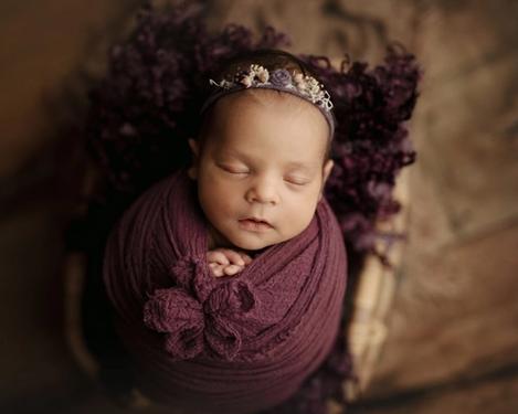 Baby mit Stirnband in einem lila farbigen Tuch eingewickelt