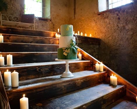 3-teilige Stocktorte in grün und weiß mit Golddeko auf rustikaler Stiege umrahmt mit brennenden Kerzen